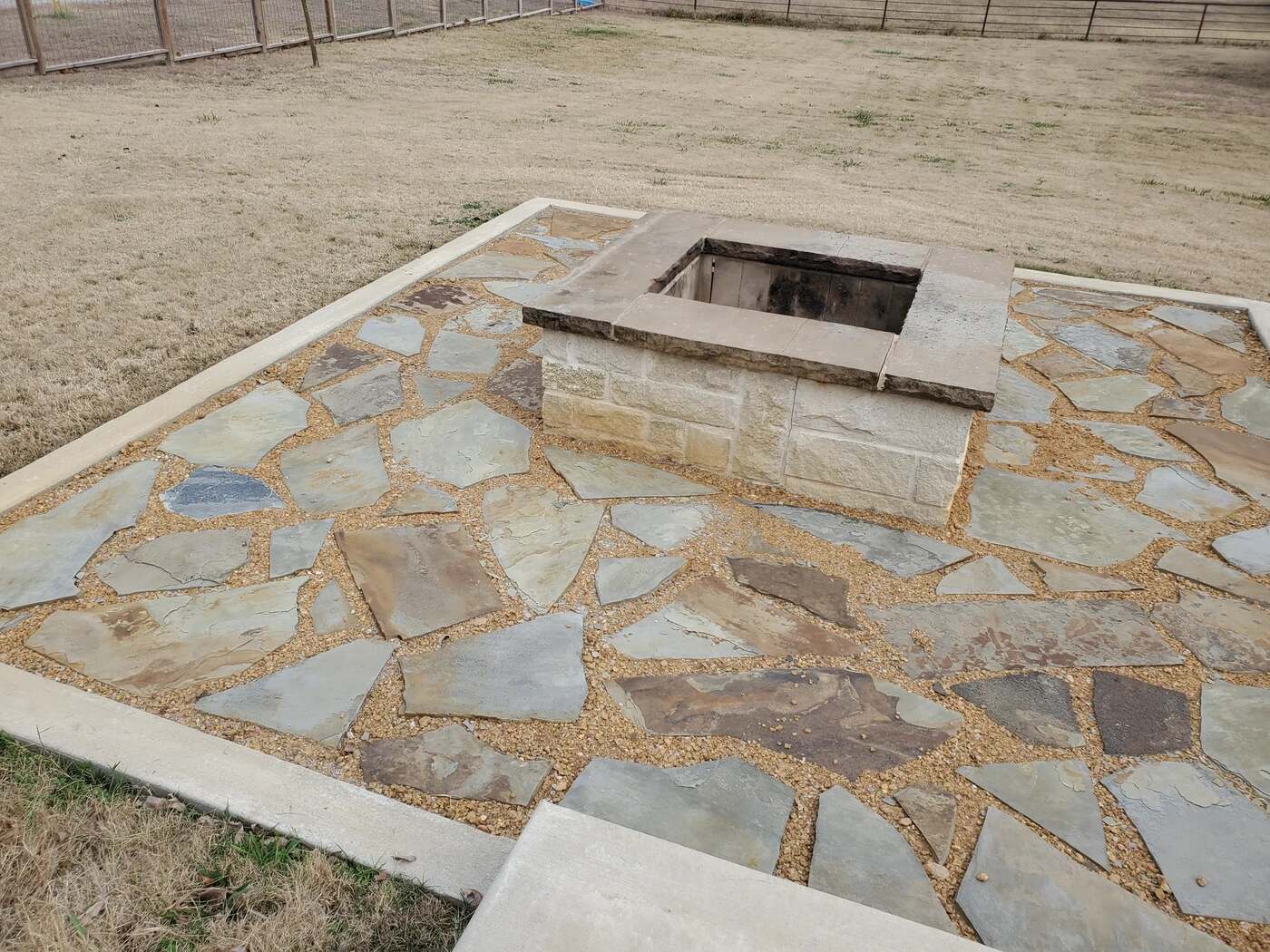 Flagstone patio with a square stone fire pit, joints filled with fine gravel