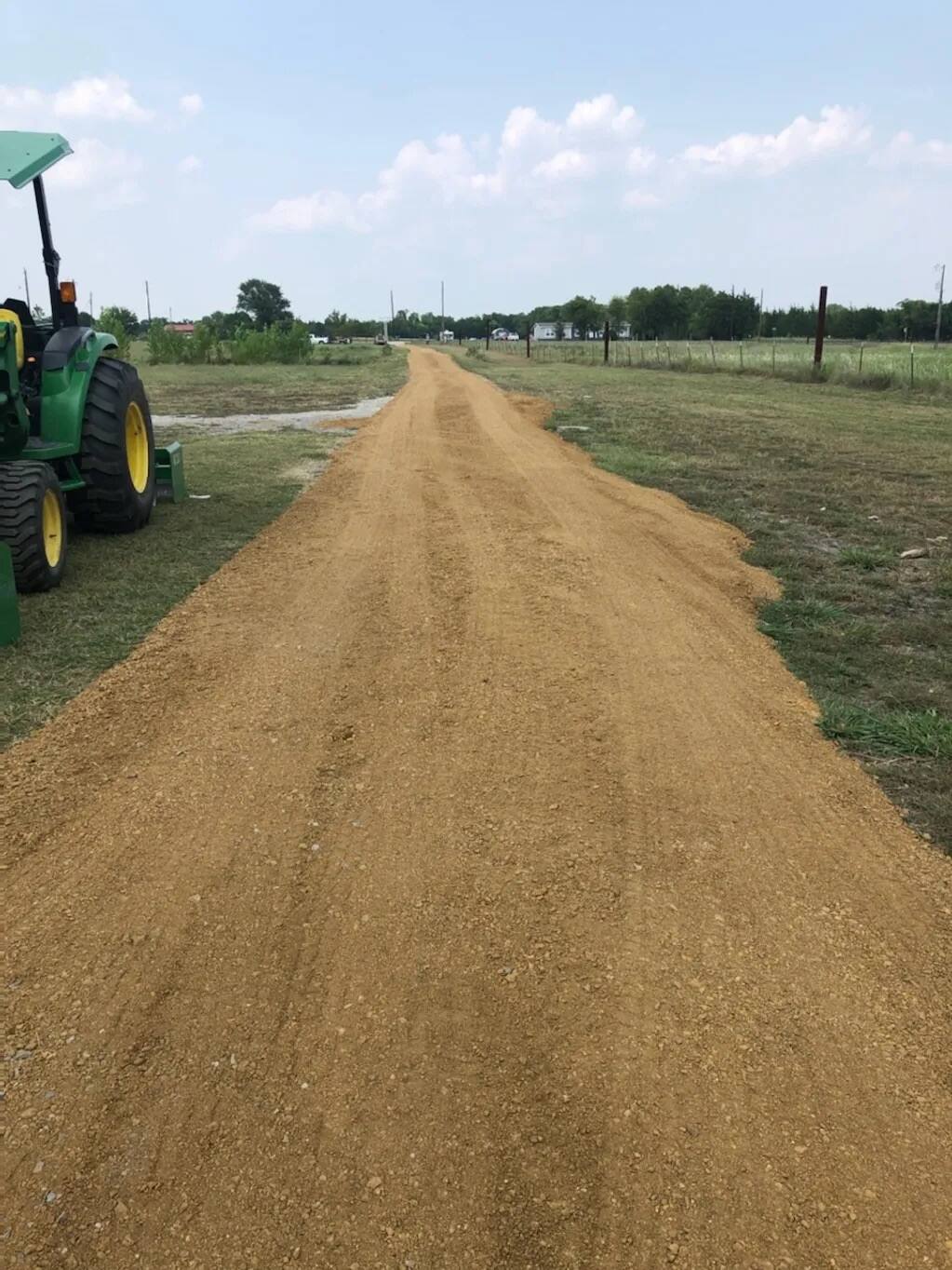 Long gravel driveway cut across pasture with a tractor parked alongside