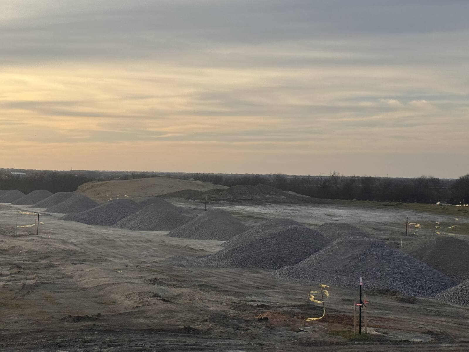 Rows of gravel loads dumped across a staked site at sunset