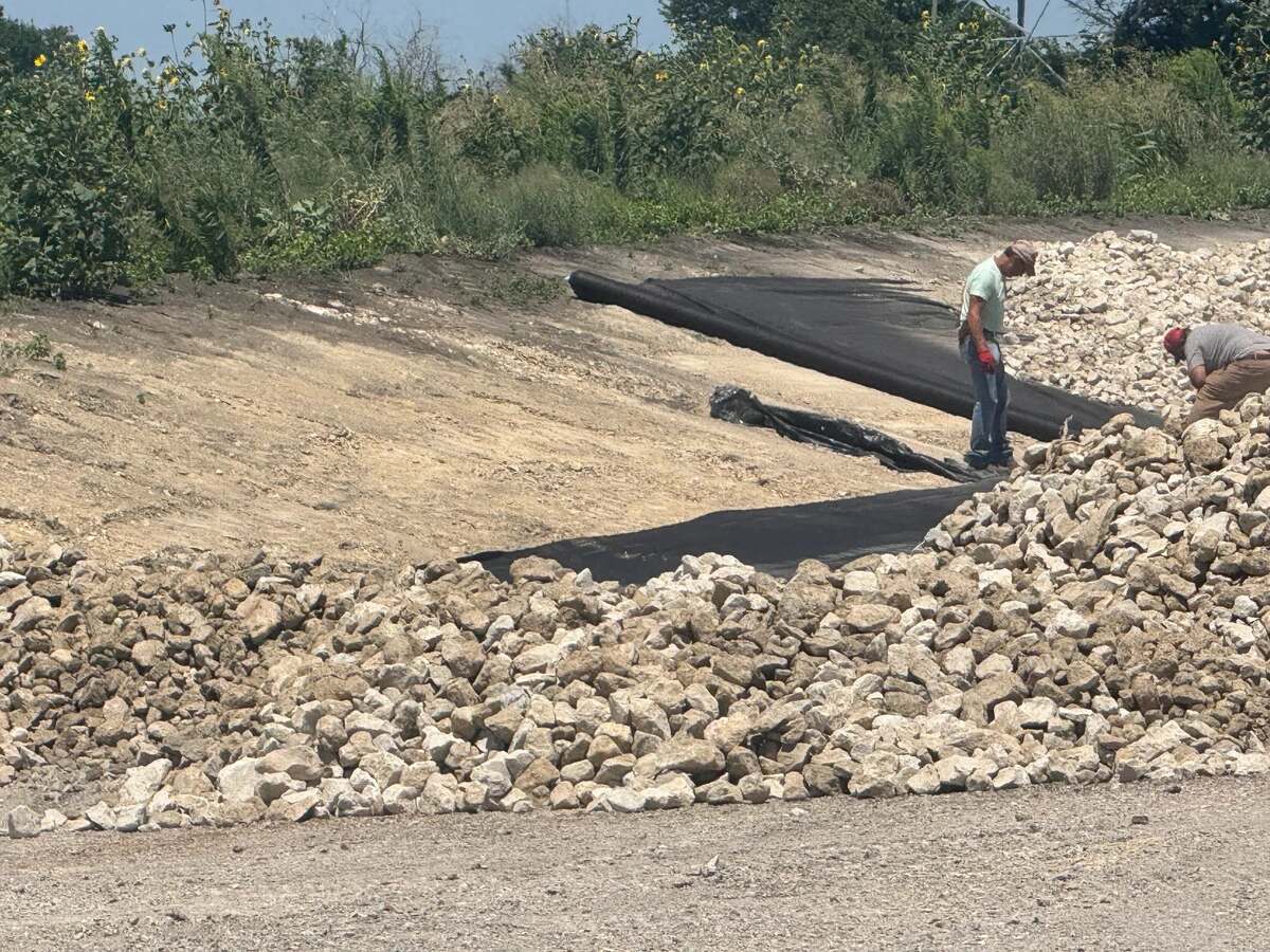 Workers rolling filter fabric down a cleared bank before placing rip rap