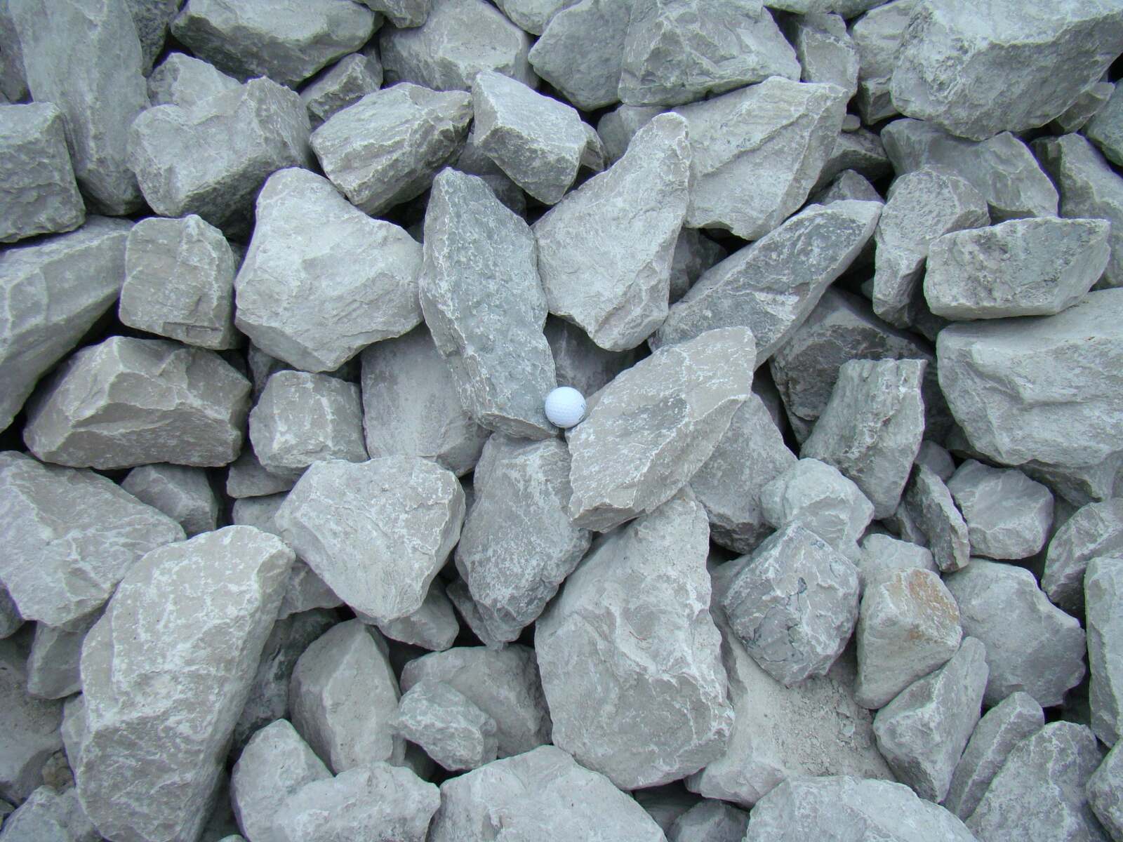 Large grey limestone rip rap with a golf ball resting on it for scale